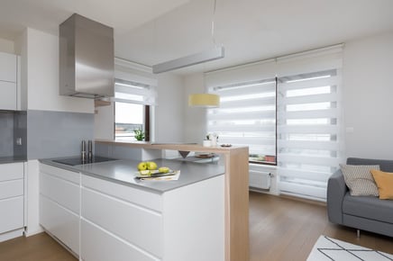 Bílá kuchyně s barem, moderní interiér s oknem a žaluziemi.